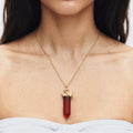 A close-up of a model wearing a delicate gold chain necklace with a gold swan pendant holding a faceted dark red Carnelian gemstone.
