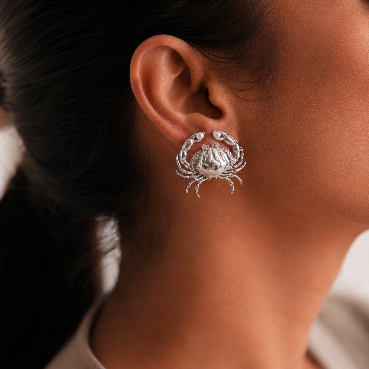 Silver crab-shaped earring worn by a women with dark hair.