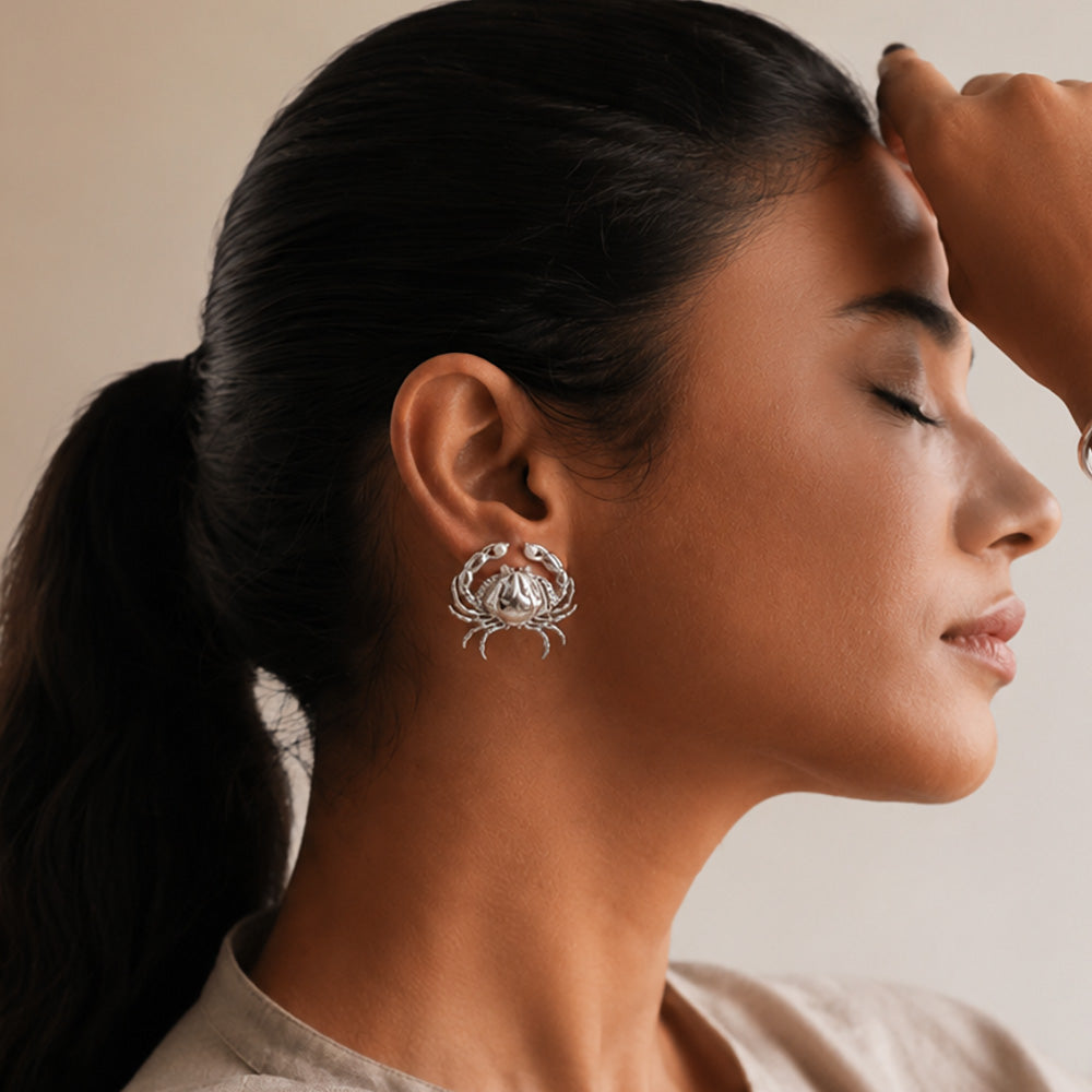 Woman wearing a silver crab earring with a neutral background