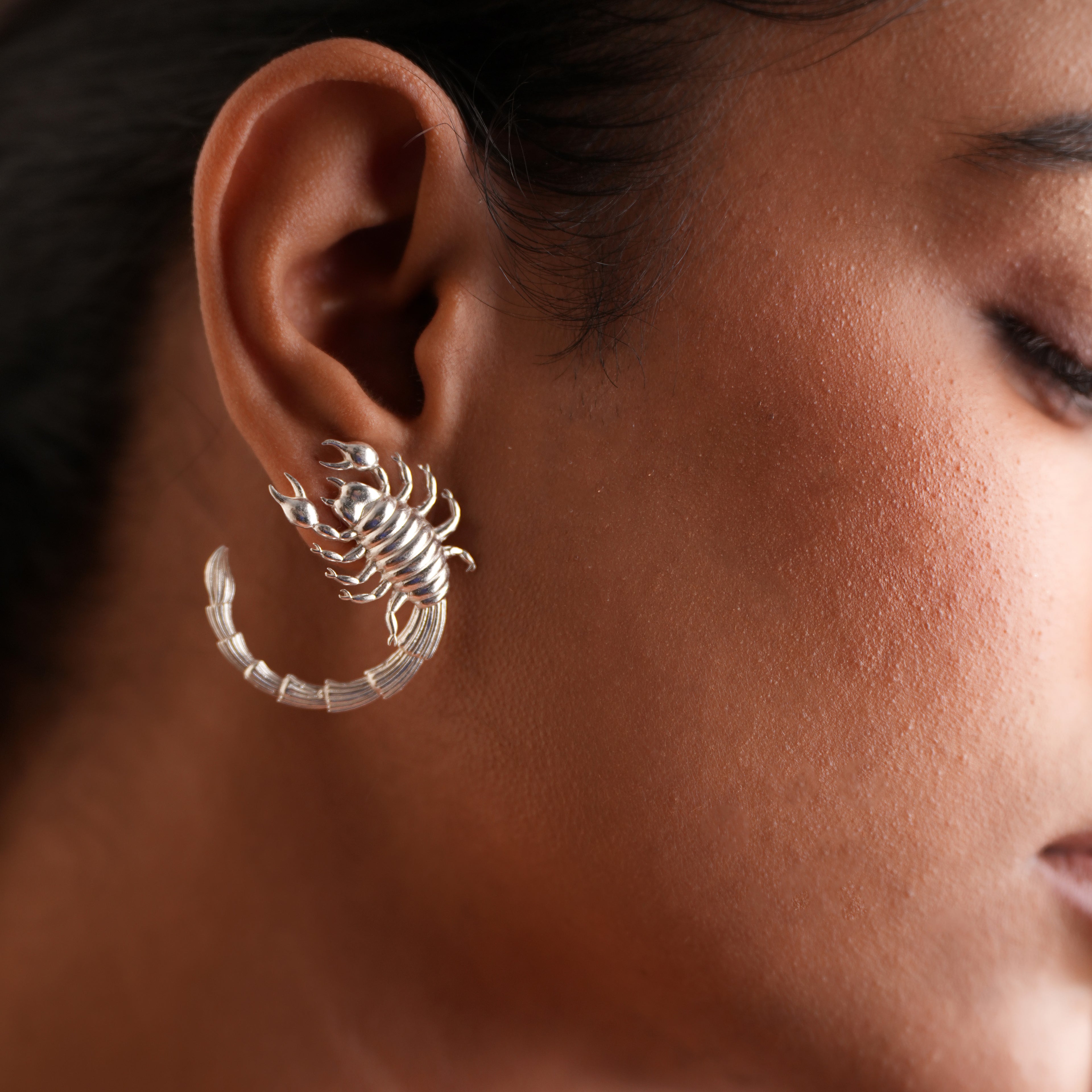 Close-up of a person wearing a silver scorpion earring.