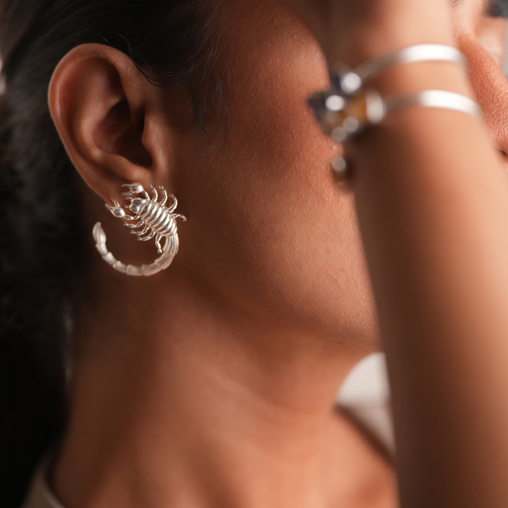 Close-up of a person wearing a silver scorpion-shaped earring.